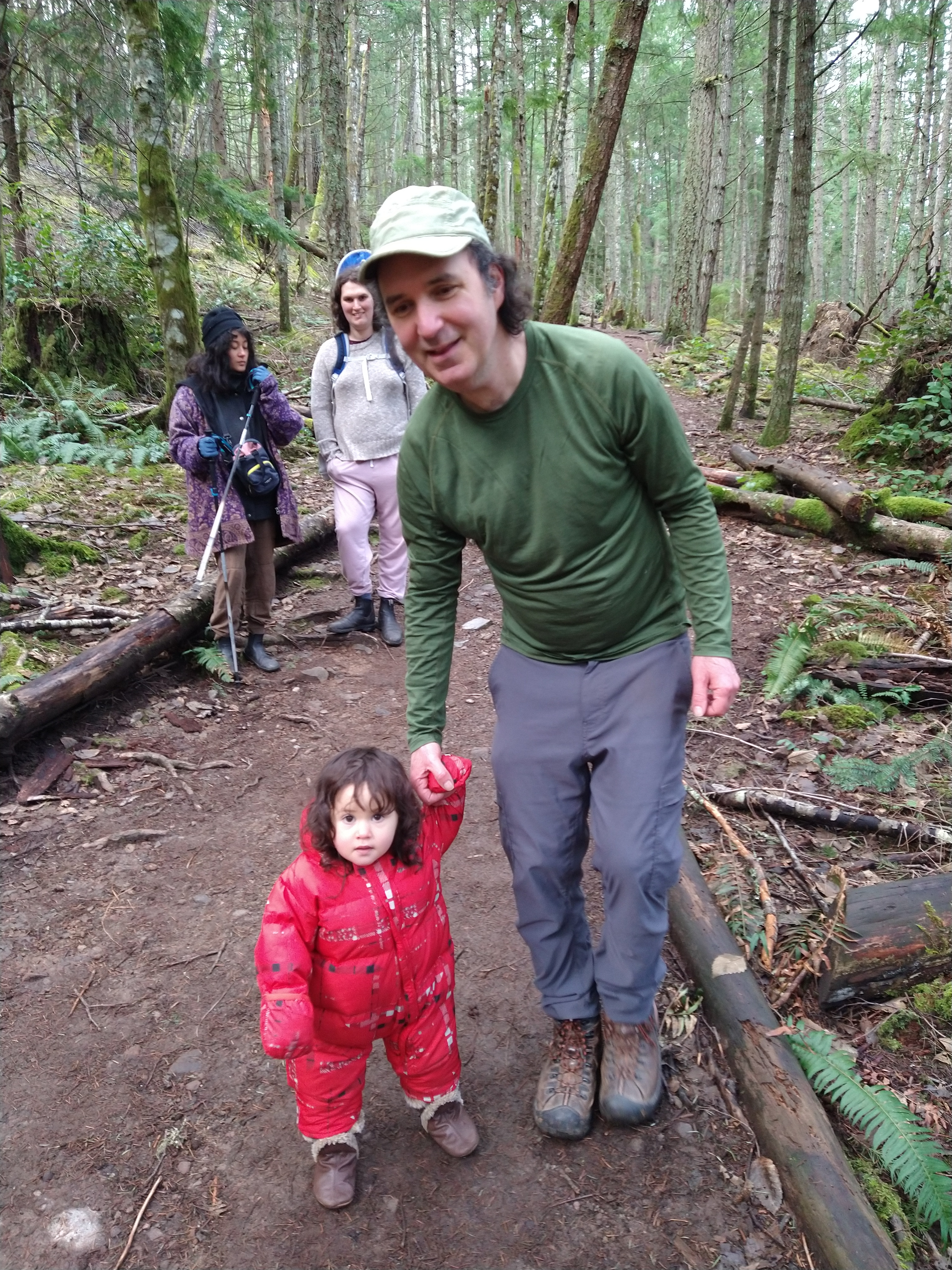 Photo of man leaning over to hold young child's hand.
